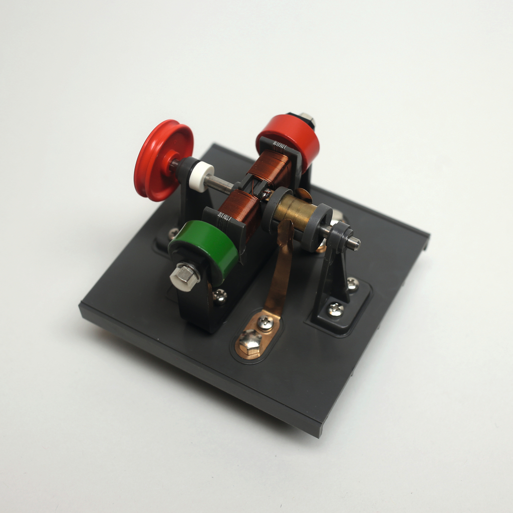 Das Bild zeigt ein Experimentiergerät, das zur Demonstration von elektromagnetischen Prinzipien verwendet wird. Es besteht aus einer Basisplatte mit verschiedenen farbigen Riemenscheiben und elektrischen Komponenten, die den Betrieb eines Elektromotors veranschaulichen.