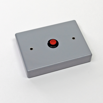 Das Bild zeigt ein graues Gehäuse mit einem roten Druckknopf in der Mitte. Es sind zwei Öffnungen auf der Oberseite sichtbar, die möglicherweise für Anschlüsse oder Sensoren gedacht sind.