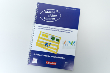 Das Bild zeigt ein Spiralheft mit dem Titel „Mathe sicher können“, das Handreichungen für Diagnose- und Förderkonzepte in der Mathematik bietet. Es behandelt Themen wie Brüche, Prozente und Dezimalzahlen und richtet sich an Lehrerinnen und Lehrer.