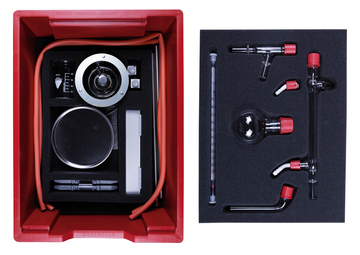 Das Bild zeigt ein Experimentierkit, das in einer roten Box verpackt ist. Der Inhalt umfasst verschiedene Glasgeräte, eine Skala und Schläuche, die für chemische Experimente im Bildungsbereich verwendet werden können.