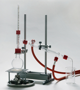 Das Bild zeigt eine chemische Apparatur, die zur Durchführung von Experimenten im Bildungswesen verwendet wird. Sie besteht aus mehreren Glasgeräten, einem Stativ und Anschlüssen für Schläuche, die in der chemischen Forschung und im Unterricht Anwendung finden.