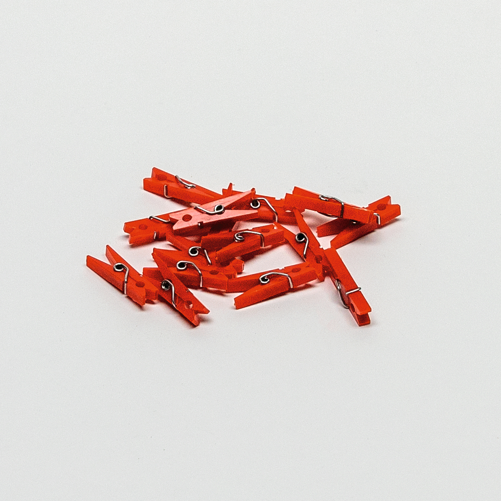 Das Bild zeigt eine Ansammlung von roten Wäscheklammern auf einem weißen Hintergrund. Diese Klammern könnten für verschiedene Experimente im Bildungsbereich verwendet werden.