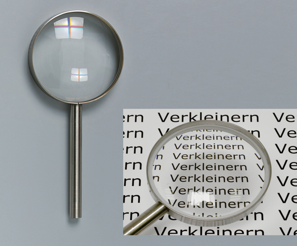 Das Bild zeigt eine Lupe mit einem klaren Glasobjektiv und einem stabilen Metallgriff. Im Hintergrund sieht man wiederholt das Wort "Verkleinern", das durch die Lupe vergrößert wird, was die Funktion des Objekts veranschaulicht.
