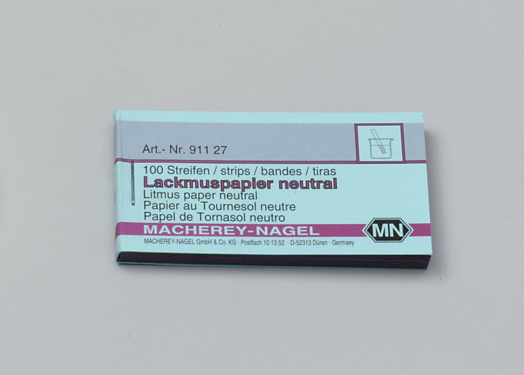 Das Bild zeigt eine Packung mit 100 Streifen neutralem Lackmuspapier, das zur pH-Wert-Bestimmung eingesetzt wird. Die Verpackung stammt von der Firma Macherey-Nagel und enthält mehrsprachige Beschreibungen der Produkteigenschaften.