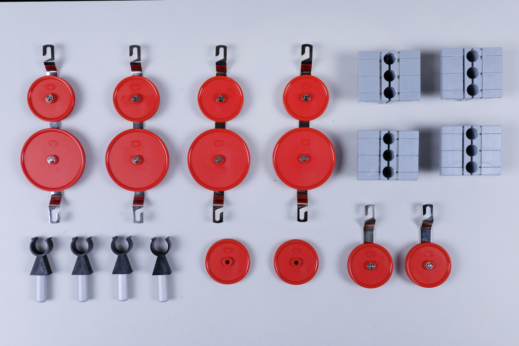 Das Bild zeigt eine Anordnung von roten Rollen und grauen Blocken, die im Experimentierbedarf verwendet werden. Diese Komponenten sind wahrscheinlich für physikalische Experimente zur Analyse von Kräften und Bewegungen gedacht.