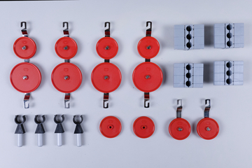 Das Bild zeigt eine Anordnung von roten Rollen und grauen Blocken, die im Experimentierbedarf verwendet werden. Diese Komponenten sind wahrscheinlich für physikalische Experimente zur Analyse von Kräften und Bewegungen gedacht.