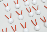 Das Bild zeigt eine Anordnung von weißen Kugeln mit roten, kurzen Stäbchen, die senkrecht herausragen. Diese Teile könnten zu einem pädagogischen Experimentierset gehören, möglicherweise zur Veranschaulichung von Molekülstrukturen oder ähnlichen Konzepten.