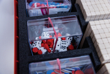 In transparent Behältern sind verschiedene Spielmaterialien wie Würfel und Holzspielsteine sortiert. Daneben liegen weitere Materialien wie kleine Kärtchen, die für mathematische Übungen oder Spiele genutzt werden können.