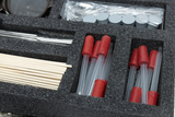 Im Kasten sind verschiedene Experimentierutensilien organisiert, darunter klare Röhrchen mit roten Stopfen, Holzstäbchen und ein Werkzeug. Die Anordnung in der schaumstoffgepolsterten Verpackung gewährleistet eine sichere Lagerung und einfachen Zugriff auf die Materialien.