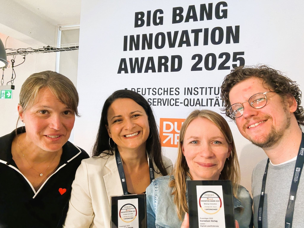 Vier Personen stehen zusammen und lächeln in die Kamera, während sie Auszeichnungen in den Händen halten. Im Hintergrund ist ein Banner mit der Aufschrift "BIG BANG INNOVATION AWARD 2025" zu sehen, das auf ein bedeutendes Ereignis hinweist.