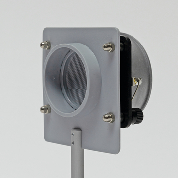 Ein graues Gerät mit einem runden Öffnungsgitter und mehreren Halterungen befindet sich auf einem stabilen Standfuß. Es scheint für experimentelle Zwecke im Bildungsbereich konzipiert zu sein, um möglicherweise Luftströmungen oder ähnliche Phänomene zu demonstrieren.