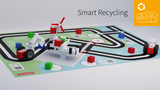 Eine bunte Spielmatte zeigt ein Recycling-Thema mit einem Straßenlayout und verschiedenen farbigen Würfeln. Darauf befinden sich robotische Modelle, die mit Bausteinen konstruiert sind und unterschiedliche Funktionen demonstrieren sollen.