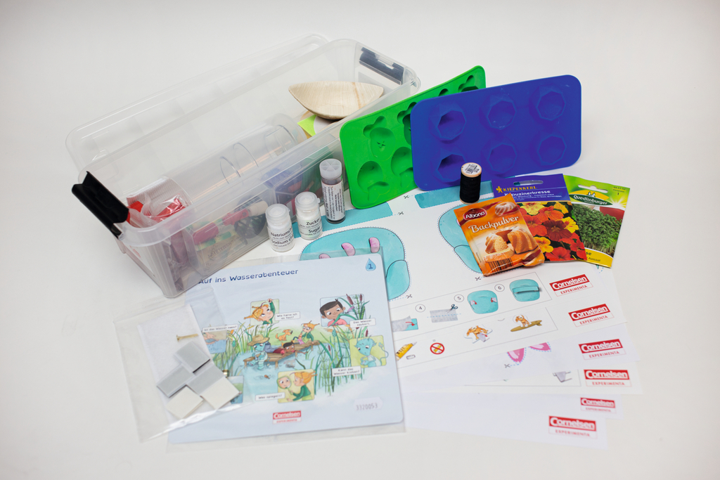 Ein Set aus Experimentierbedarf umfasst eine Kunststoffbox, Formschalen, Reagenzgläser und verschiedene Pulver. Ergänzt wird das Set durch detaillierte Anleitungen und Informationsblätter des Herstellers Cornelsen.