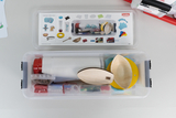 Ein Set für Physikexperimente liegt in einer transparenten Kunststoffbox. Die enthaltenen Utensilien wie Holzformen und Kunststoffteile sind auf dem Deckel abgebildet.