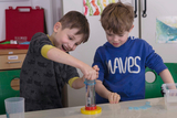 Zwei Jungen führen konzentriert ein naturwissenschaftliches Experiment an einem Tisch durch. Ein Junge bedient dabei eine transparente Apparatur mit einem gelben Sockel.