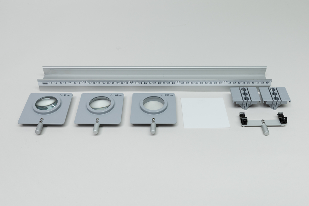 Ein Set aus drei verschiedenen Sammellinsen mit Halterungen liegt neben einer metrischen optischen Bank. Ergänzt wird das Set durch einen weißen Bildschirm sowie passende Befestigungsklemmen.