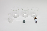Ein Set aus drei Bechergläsern, einem Erlenmeyerkolben, einem Glasstab und einem Reagenzglas ist auf weißem Grund angeordnet. Die Laborgeräte bestehen überwiegend aus transparentem Glas.