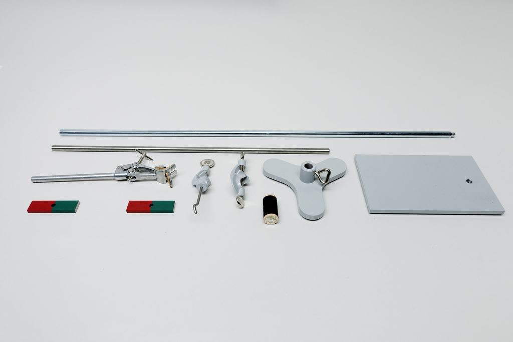 Ein Set aus physikalischen Experimentierutensilien liegt auf weißem Grund. Es umfasst Metallstangen, Klemmen, Magnete sowie eine graue Basisplatte.