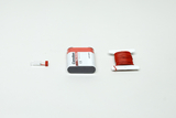 Eine 4,5V-Flachbatterie liegt neben einer Spule mit rotem Isolierdraht. Links daneben befindet sich eine kleine, transparente Kunststoffhülse.