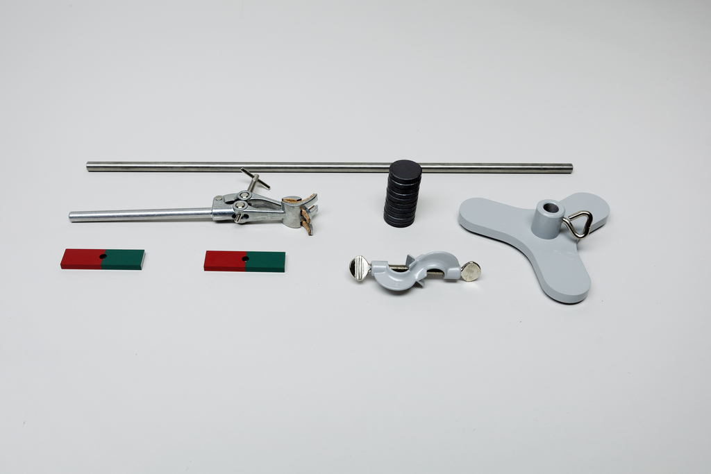 Ein Set aus Physik-Experimentiermaterial liegt auf weißem Grund. Es umfasst eine Stange, Gewichte, eine Halterung, Klemmen sowie zwei rot-grüne Magnete.