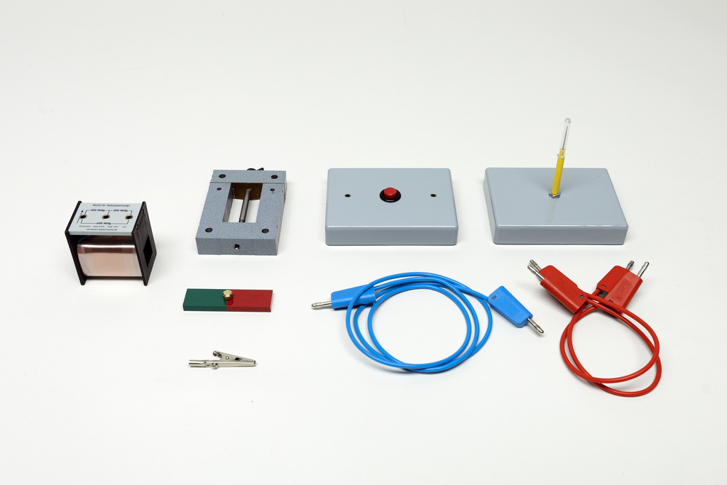 Ein Physik-Experimentierset enthält verschiedene elektrische Komponenten wie eine Spule, einen Schalter und Anschlusskabel. Ergänzt wird das Set durch einen Stabmagneten sowie eine Halterung.