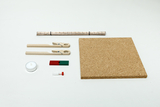 Ein Set aus Experimentierbedarf umfasst eine Korkplatte, Holzklammern und ein Bündel Strohhalme. Ergänzt wird das Ensemble durch ein Teelicht, ein kleines Reagenzglas und einen zweifarbigen Holzblock.
