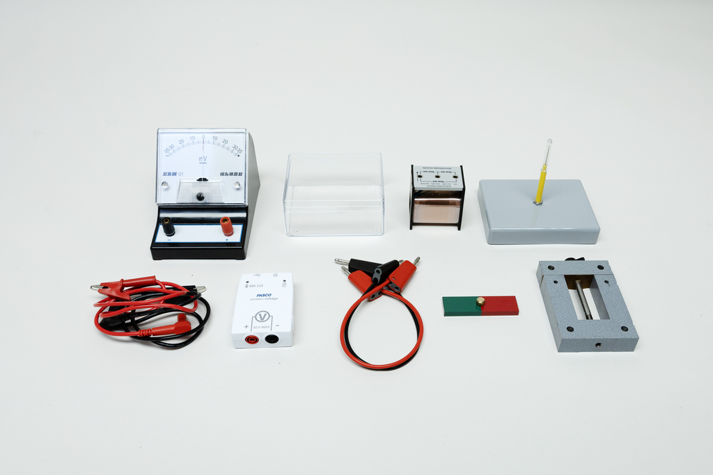 Ein Physik-Experimentierset mit Galvanometer, Kabeln und Magneten liegt auf weißem Grund. Die Anordnung umfasst zudem diverse Messgeräte und Zubehör für den Schulunterricht.
