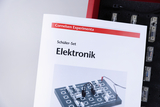 Ein Handbuch des „Cornelsen Experimenta Schüler-Sets“ für Elektronik steht im Vordergrund. Es zeigt auf dem Cover ein Beispiel für einen elektronischen Versuchsaufbau.