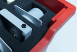 Ein roter Koffer enthält verschiedene technische Komponenten, die sicher in schwarzem Schaumstoff fixiert sind. Eines der silbernen Bauteile trägt die Beschriftung „12V/20W“.
