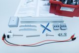 Ein Physik-Experimentierset zur Energieumwandlung liegt mit Anleitung und roter Box bereit. Zu sehen sind elektrische Komponenten, ein blauer Propeller, Metallstäbe und Anschlusskabel.
