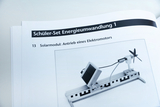 Eine geöffnete Anleitung zeigt ein Schüler-Set zur Energieumwandlung. Abgebildet ist ein Solarmodul, das einen kleinen Elektromotor mit Propeller antreibt.