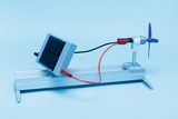 Ein kleines Solarmodul ist über zwei Kabel mit einem Elektromotor verbunden. Dieser treibt einen blauen Propeller an und dient als Versuchsaufbau zur Energiegewinnung.