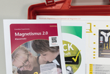 Ein Lehrerhandbuch zum Thema „Magnetismus 2.0“ liegt über einem Arbeitsheft und einer Materialliste. Im Hintergrund ist ein roter Koffer mit dem entsprechenden Klassensatz zu sehen.