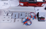 Ein Physik-Experimentierkasten zeigt verschiedene Messinstrumente, Kabel und Halterungen auf einer hellen Fläche. Im Hintergrund liegen eine Anleitung sowie die rote Transportbox des Sets.