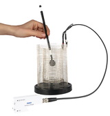 Eine Hand hält einen Sensor in einen zylindrischen Metallkäfig. Das Gerät ist über ein Kabel mit einem weißen PASCO-Messmodul verbunden.
