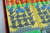 Ein Sortiment aus farbigen Kunststoffkugeln und Verbindungsstücken liegt in einem gelben Kunststoffkasten. Diese Bauteile dienen dem Modellbau von Molekülen im Chemieunterricht.