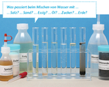 Sechs Reagenzgläser in einem Ständer enthalten Wasser, das mit verschiedenen Stoffen wie Salz, Sand, Essig, Öl, Zucker und Erde gemischt wurde. Darüber steht die Frage, was beim Mischen dieser Substanzen passiert.