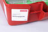 Ein roter Kunststoffkoffer enthält Laborzubehör für den Bildungsbereich. Ein Etikett weist den Inhalt als Klassensatz an Keimungsgeräten von Cornelsen Experimenta aus.