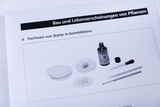 Ein Lehrbuch zeigt ein Experiment zum Nachweis von Stärke in Keimblättern. Zu sehen sind eine Petrischale, eine Lösung in einer Flasche sowie verschiedene Laborutensilien.