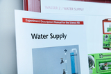 Eine Anleitung für ein Experimentierset zum Thema Wasserversorgung ist im Fokus. Im Hintergrund ist ein entsprechend beschriftetes Modul zu sehen.